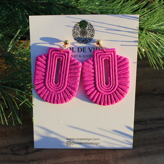 Pink earrings on a branded card with a Christmas tree in the background
